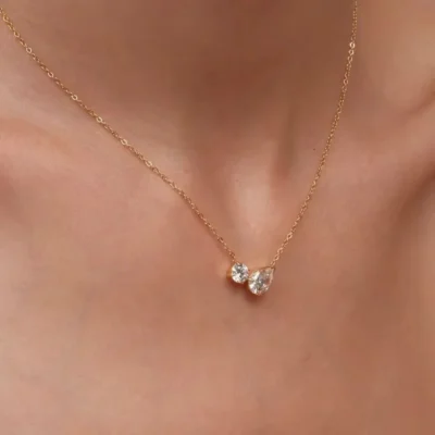 Delicate gold necklace with round and pear-shaped stone pendant on neck