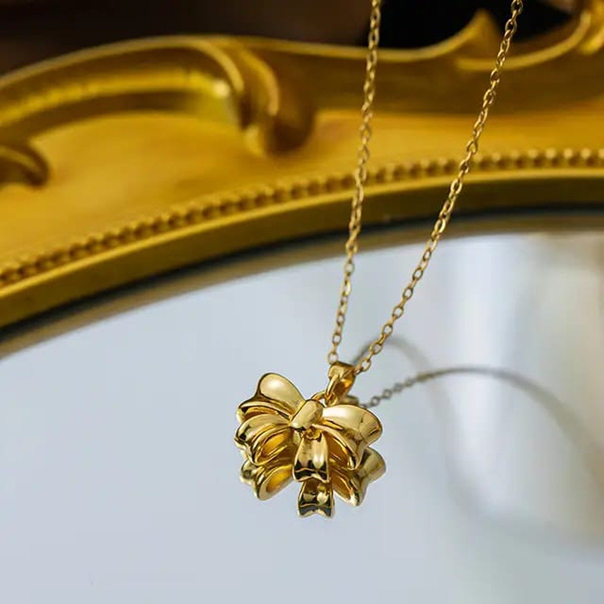 Gold-tone stainless steel bow pendant necklace on fine chain against fabric background